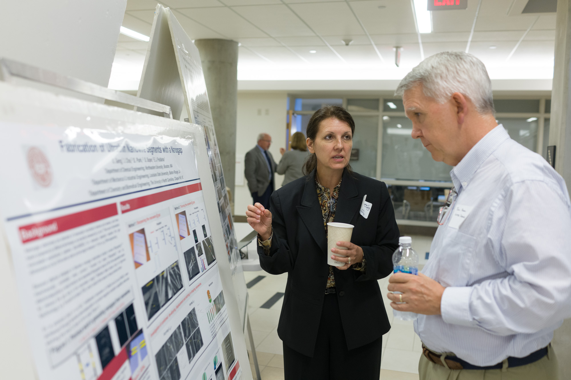 A woman named Eleanor discusses a scientific poster with a man at a conference.