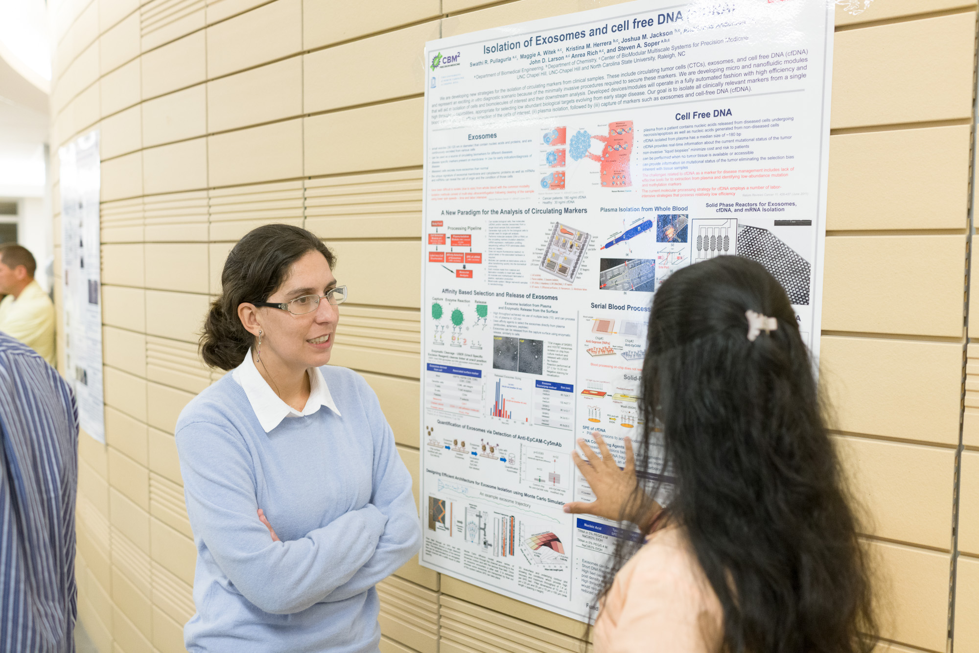 A researcher engages in a discussion about her scientific poster with another attendee at an event.