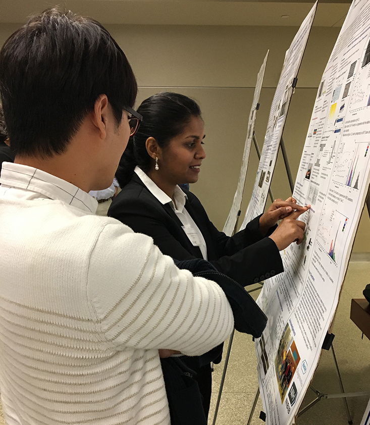 Two individuals standing in front of a research poster, engaged in discussion.