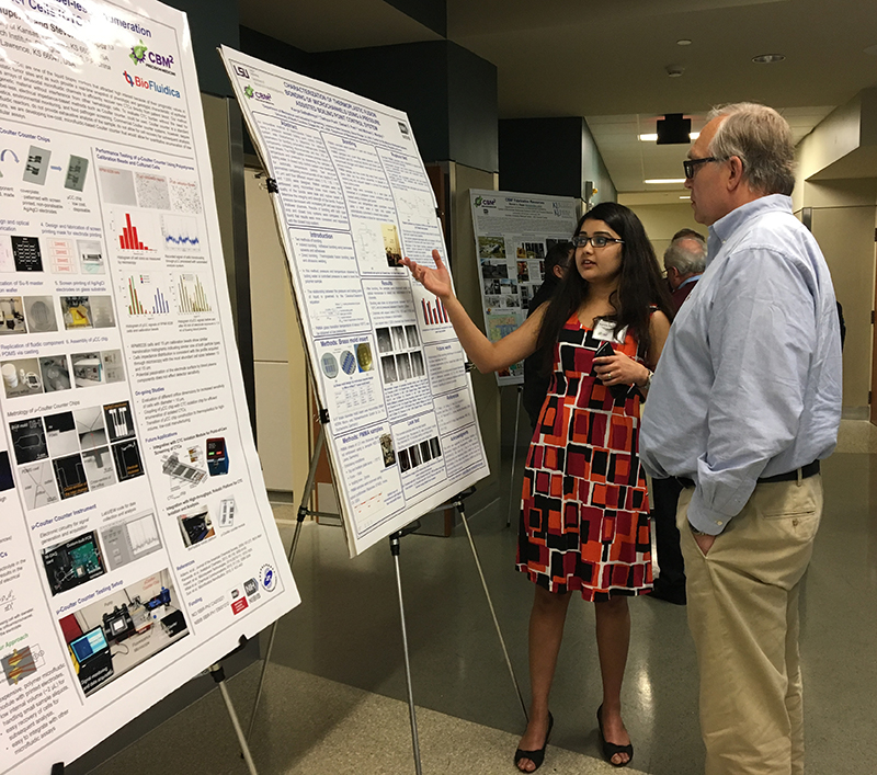 Two people discussing a research poster, with one person pointing, and two additional research posters visible—one in the foreground and one in the background.