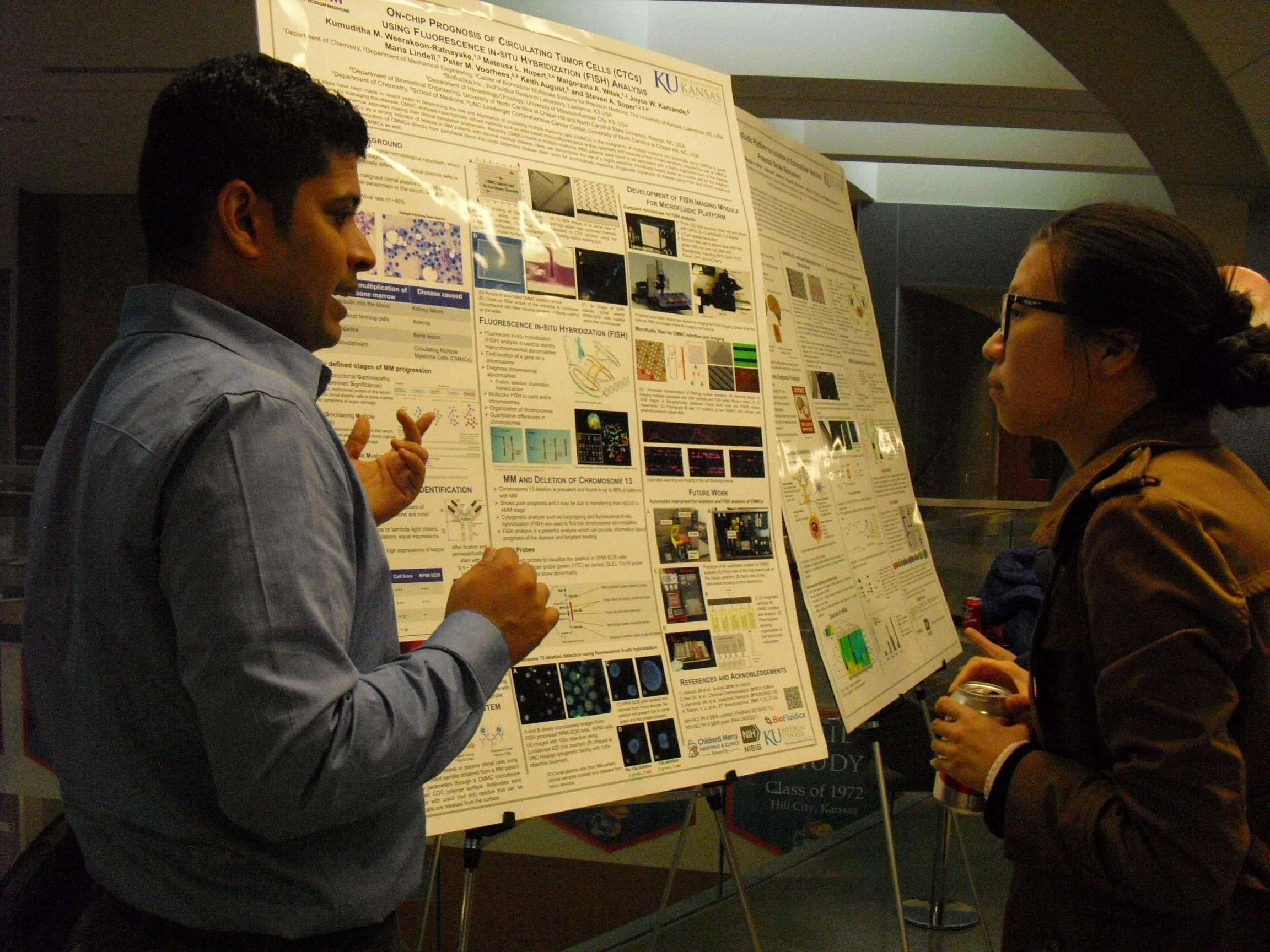 Two people in front of a research poster, one explaining its content to the other.