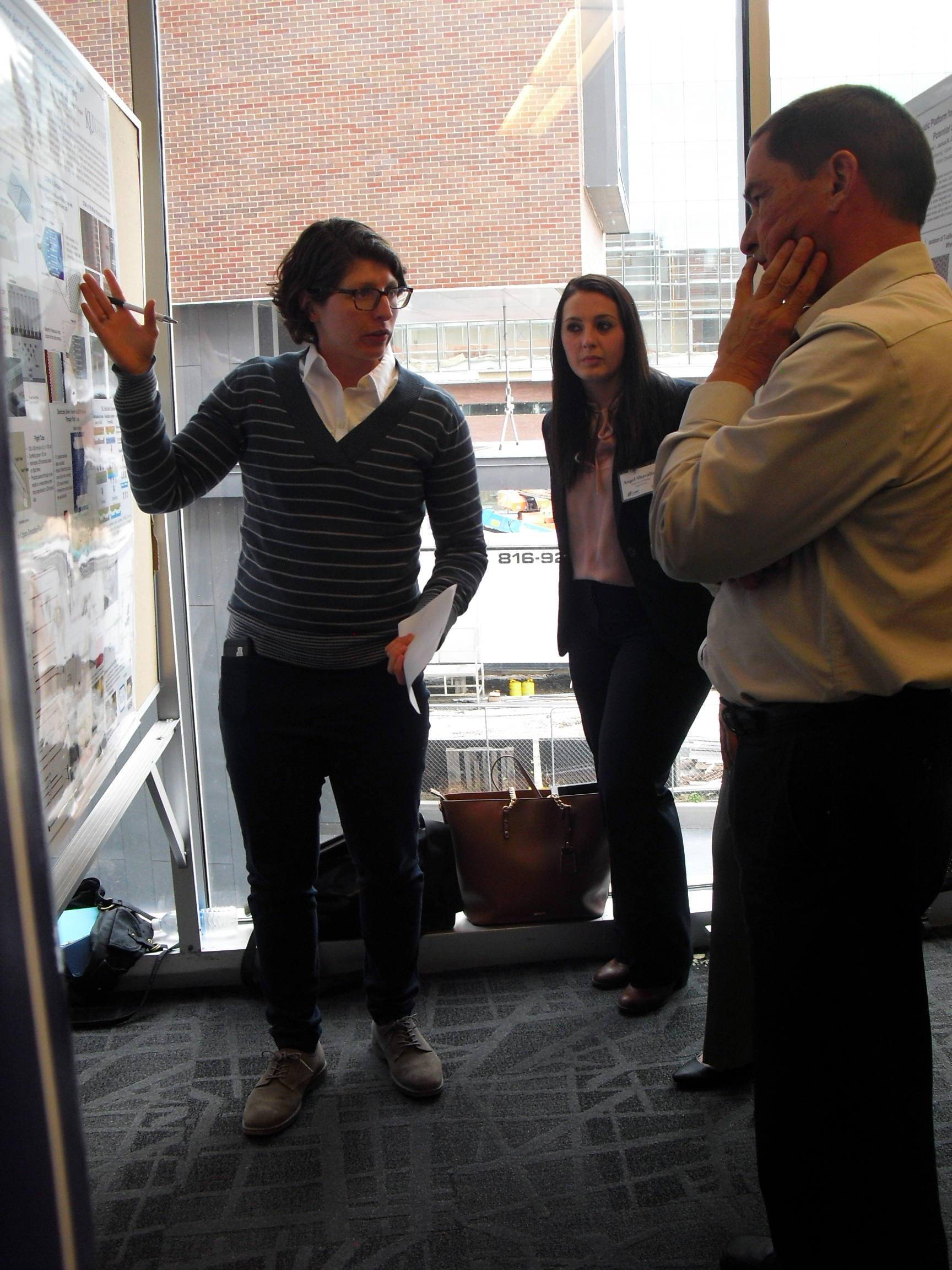One individual explaining the details of their research poster to two attentive listeners.