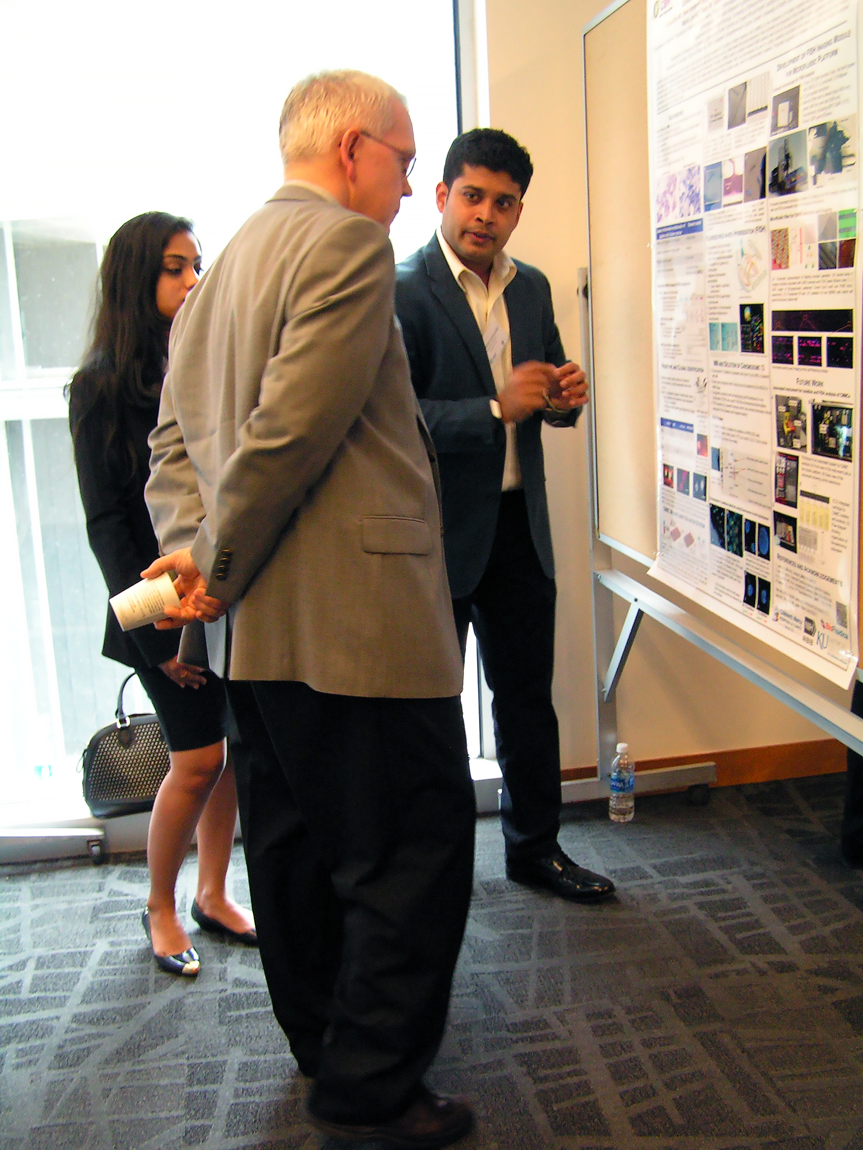 Three people standing in front of a research poster, one of them explaining its contents.