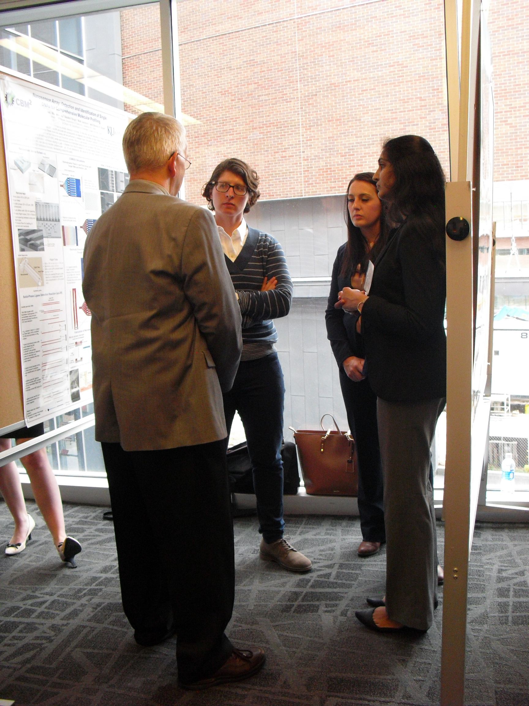 Four individuals engaged in a discussion while standing between two research posters.