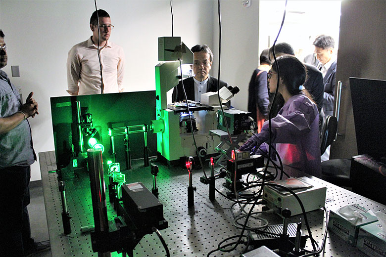 (from left) Dr. Kumuditha Ratnayake, Dr. Matt Jackson, and Dr. Teruhisa Ueda listen to graduate student Swarnagowri Vaidyanathan talk about how she uses the laser microscope